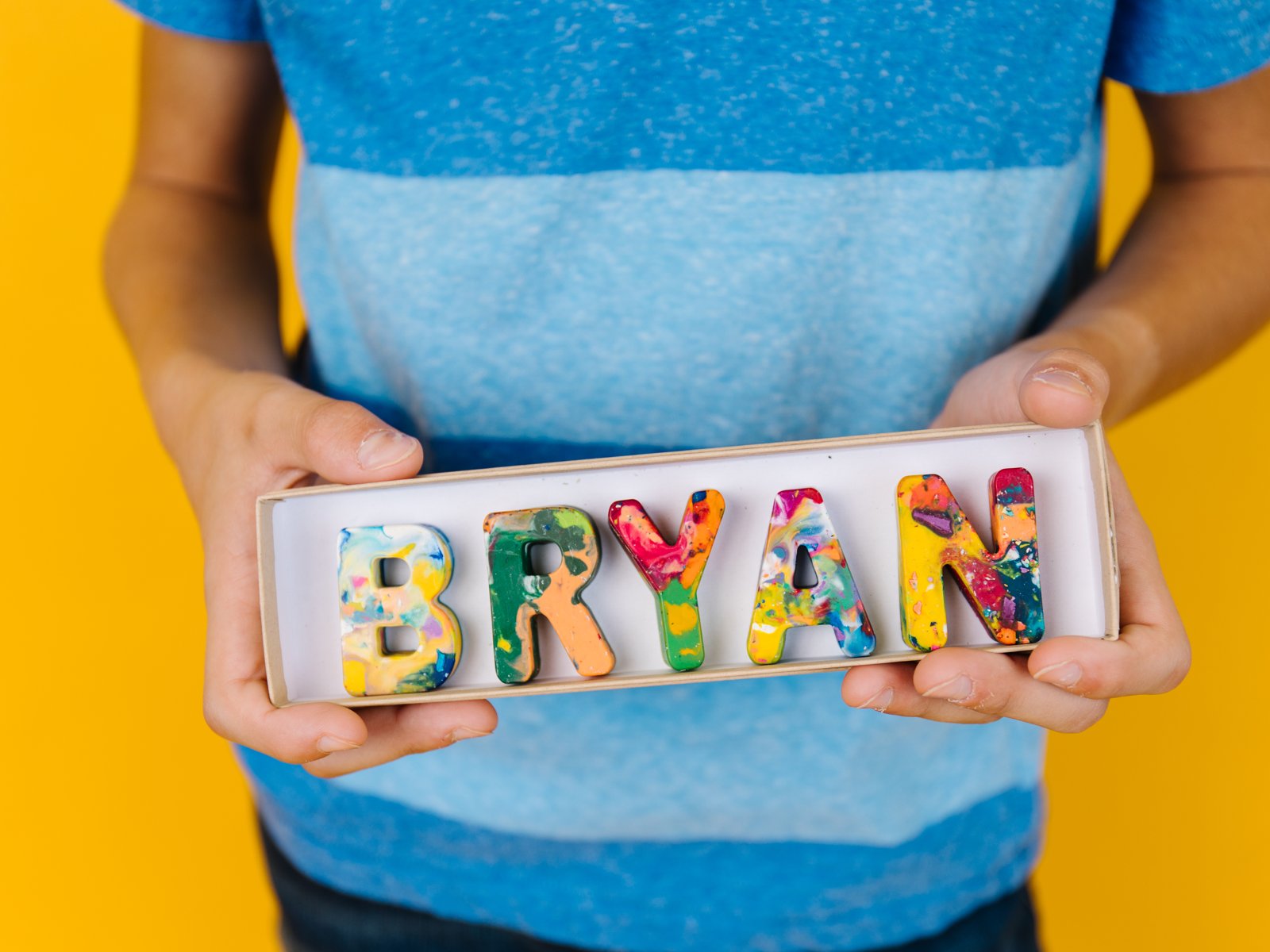 Child holding the name BRYAN spelled in rainbow crayon letters in the 8 inch box