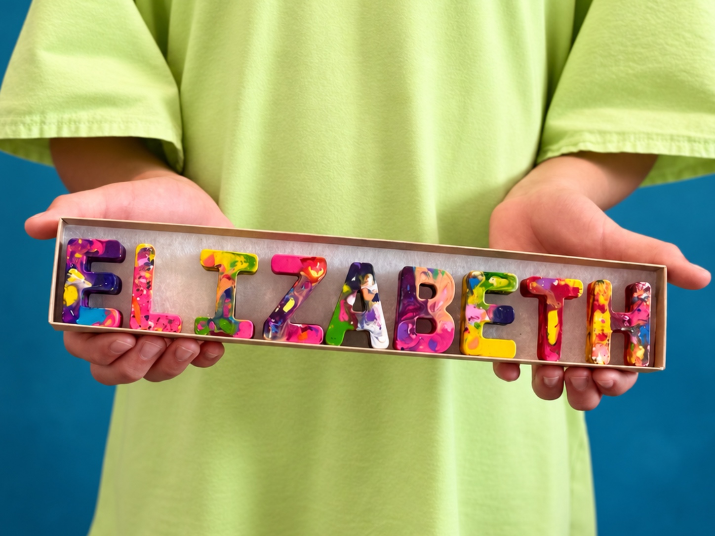 Child holding the name ELIZABETH spelled in rainbow crayon letters across the 12 inch box