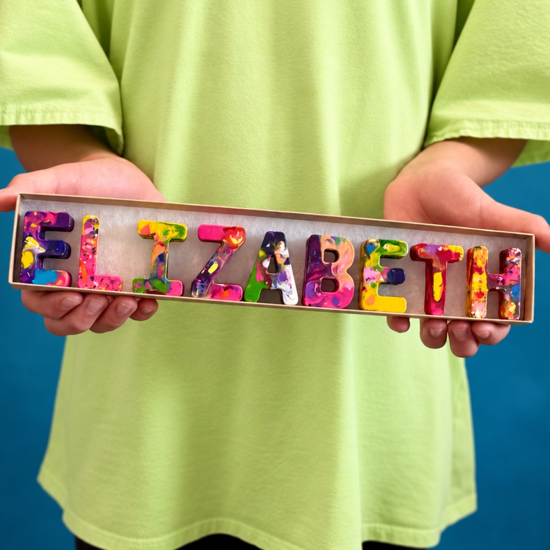 Child holding out the long name ELIZABETH spelled in rainbow crayon letters across a single row