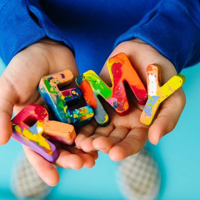 Child's hands holding the name REMY spelled in rainbow crayon letters