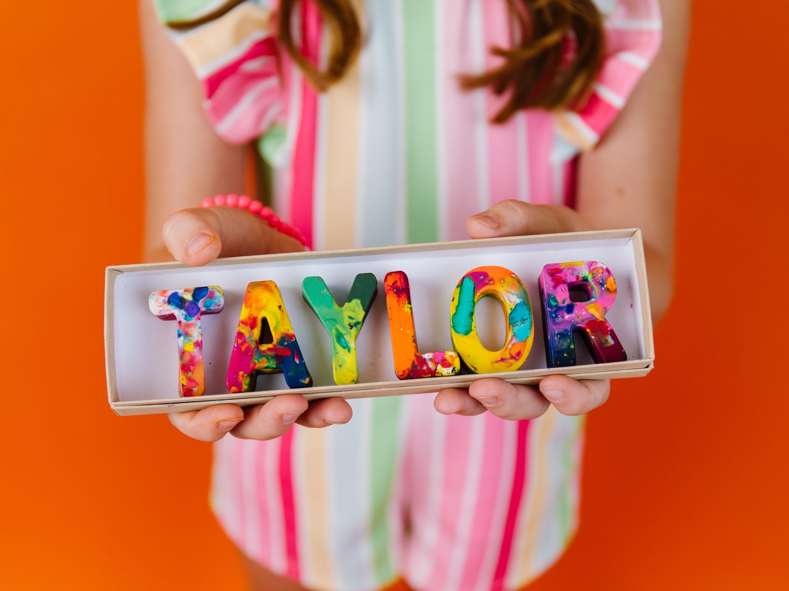 Child holding a personalized crayon name gift set spelling TAYLOR in colorful handmade crayon letters